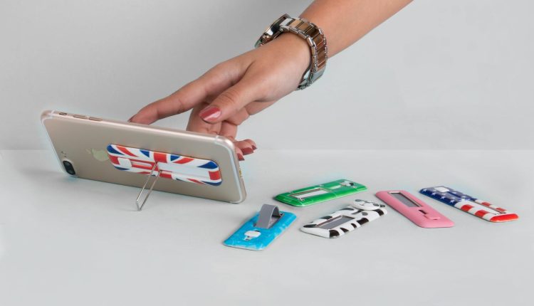 Female hand using a smartphone stand with various decorative designs on a table.