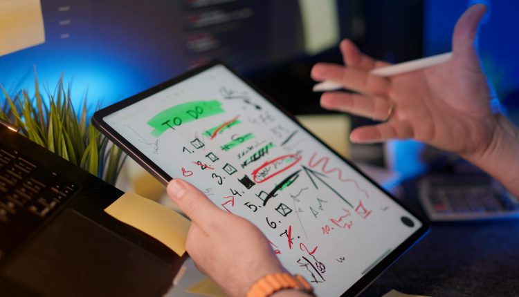 A person managing tasks on a tablet with a digital pen in a modern office setting.