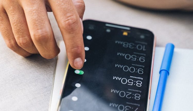 Hand adjusting alarms on smartphone screen with pen nearby in natural light.