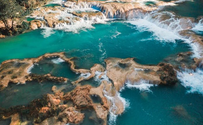 A breathtaking aerial view of stunning turquoise waterfalls amidst lush greenery.